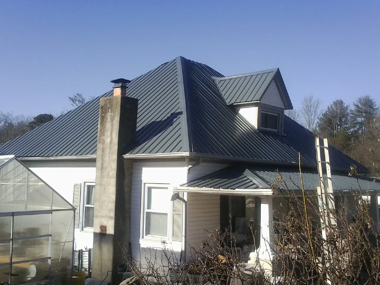 Dark blue standing seam metal roof on a white farmhouse with dormer — Slate & Tile Roof Repair by Roofing Brothers in Westgate
