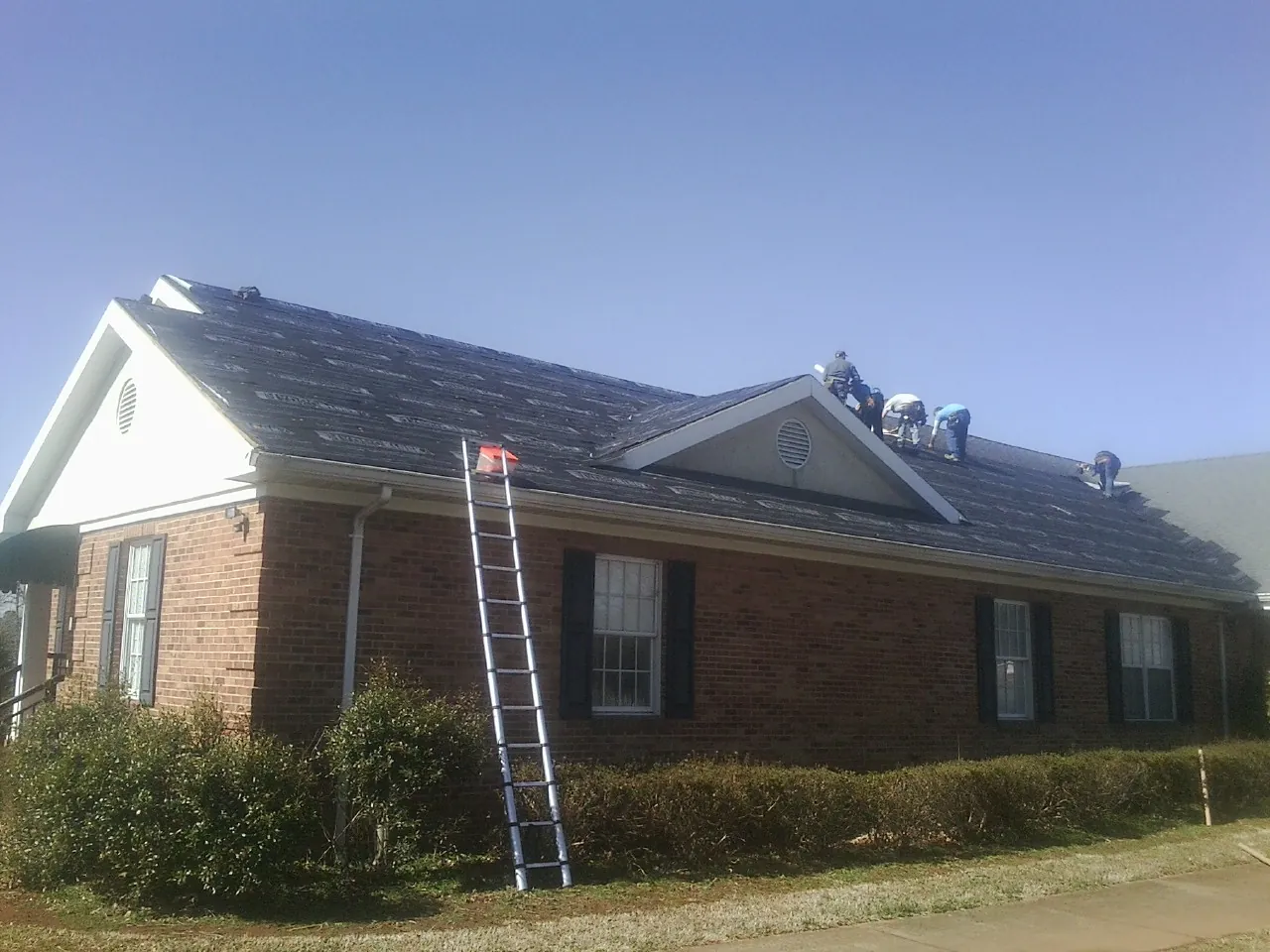 Crew tearing shingles off a brick ranch roof with a ladder set — Metal Roof Repair work by our crew in Westgate