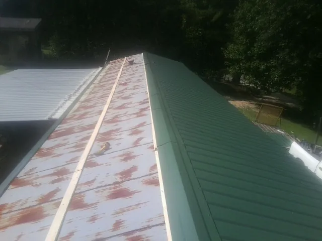 Old rusted panels beside newly installed green metal roofing — Wind Damage Roof Repair by Roofing Brothers in Westgate