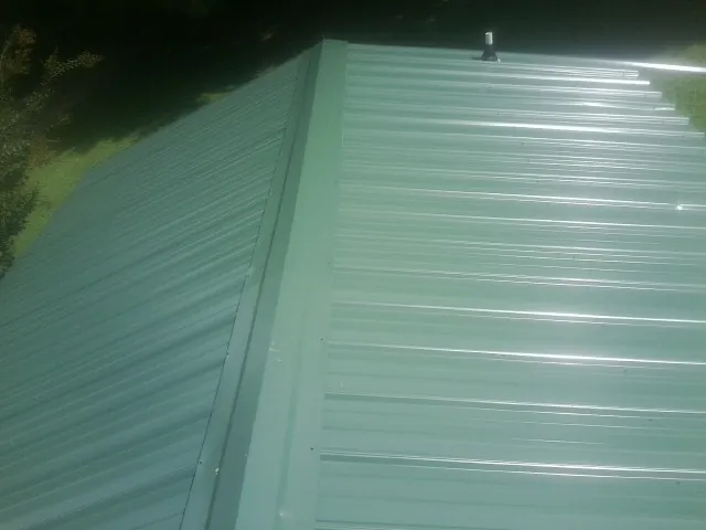 New green metal panels meeting at the ridge of a roof — Flat Roof Repair work by our crew in Westgate