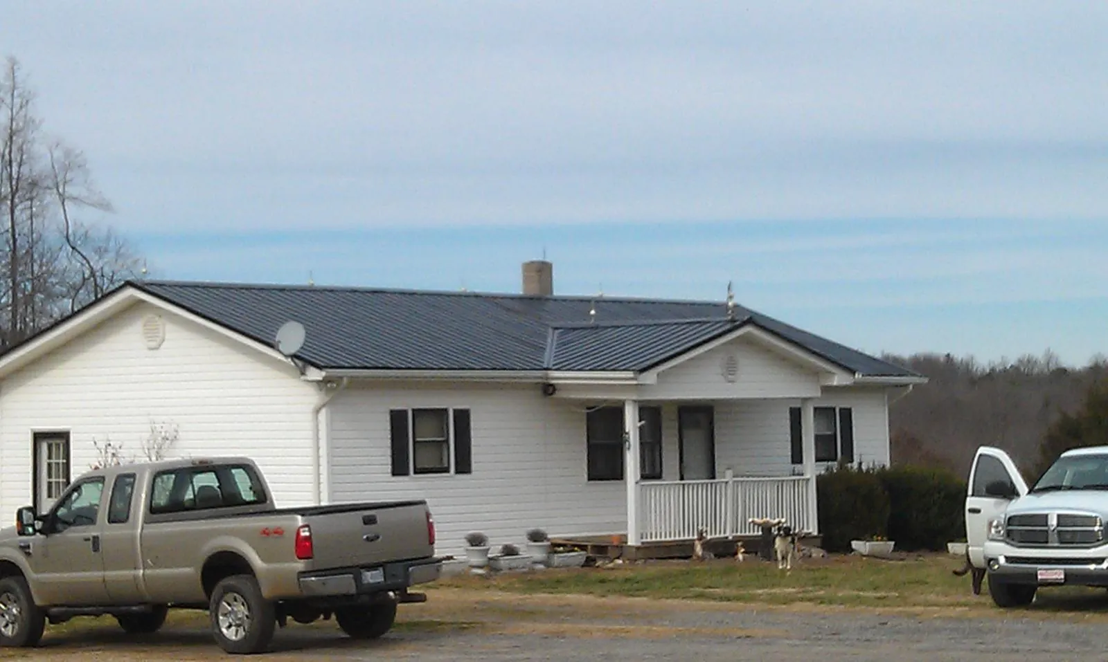 Finished dark metal roof on a white ranch home with work trucks parked in Westgate