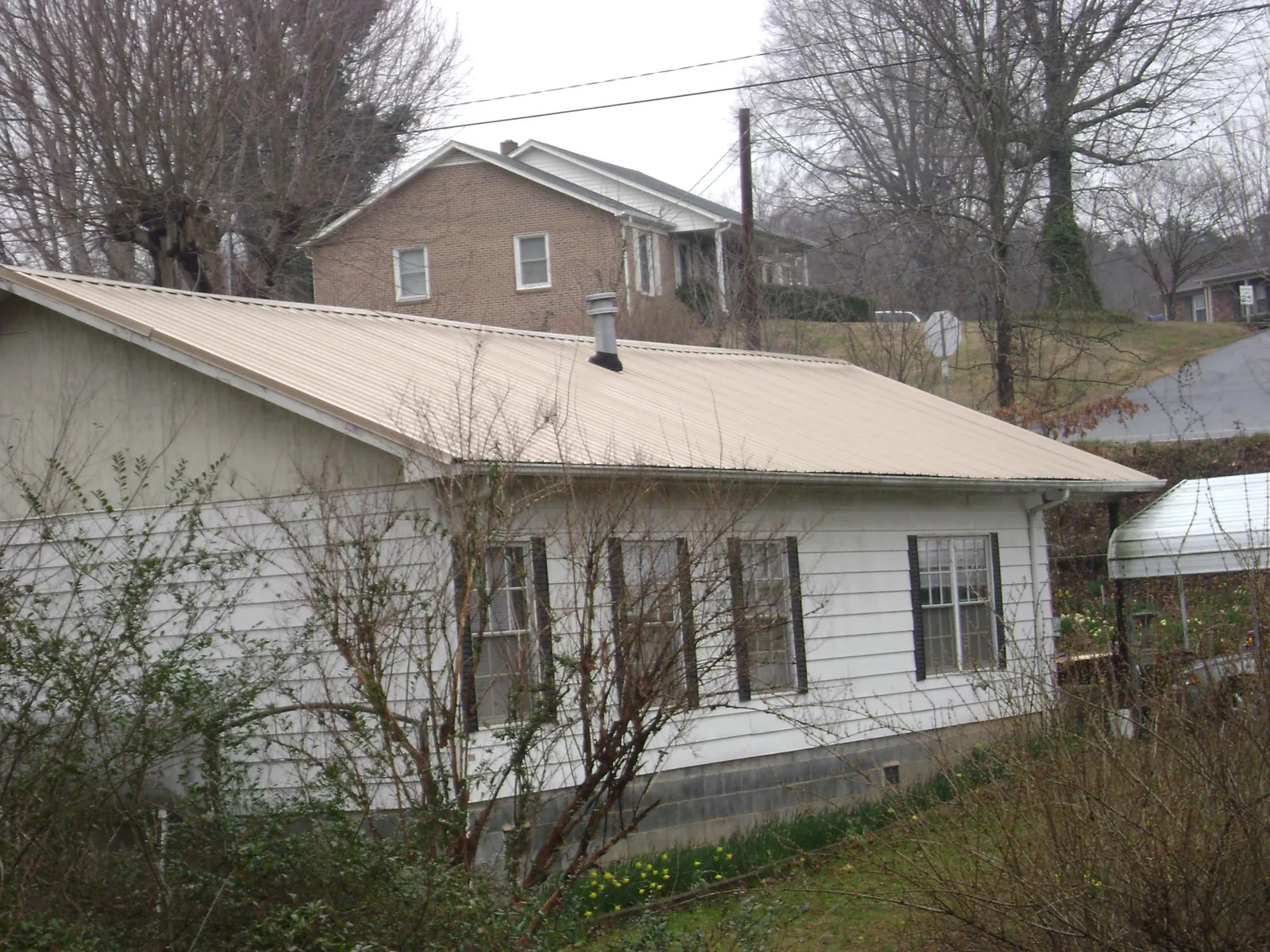 Tan metal roof on a white sided house set into a hillside — Commercial Roofing by Roofing Brothers in Westgate