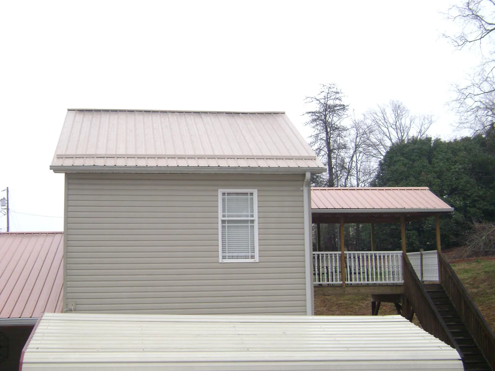 Tan metal roofs on a two story addition and attached porch, from a Roof Replacement job in Westgate